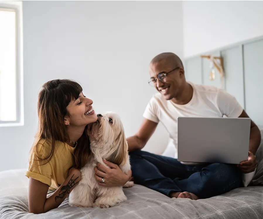 Man holding a laptop, woman holding a dog, sitting on a bed