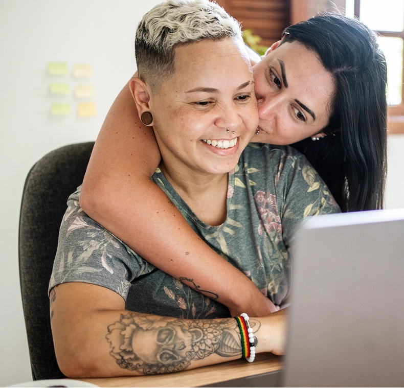 Two women embracing sitting in front of a laptop embracing
