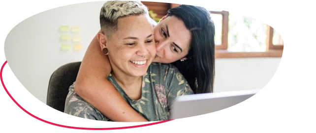 Two women embracing sitting in front of a laptop embracing